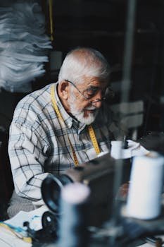 Home Senior man sewing in a workshop with sewing machine and measuring tape.